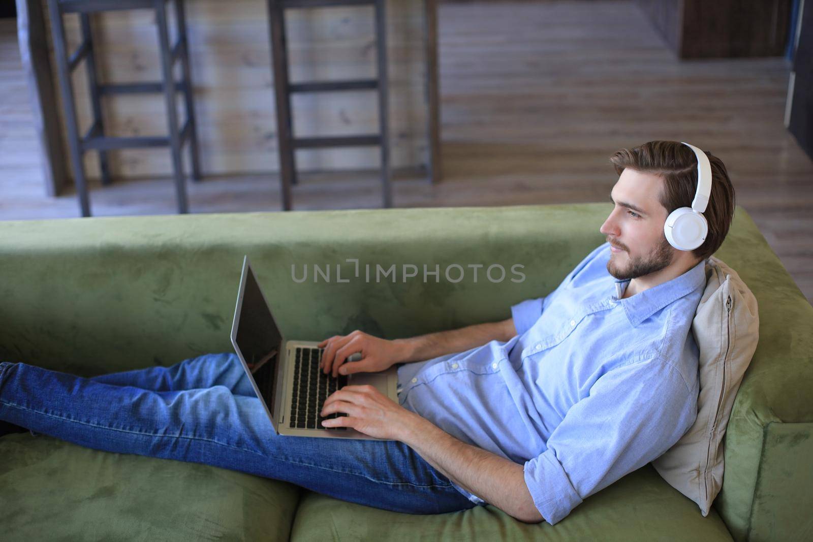 Concentrated young freelancer businessman sitting on sofa with laptop, working remotely online at home
