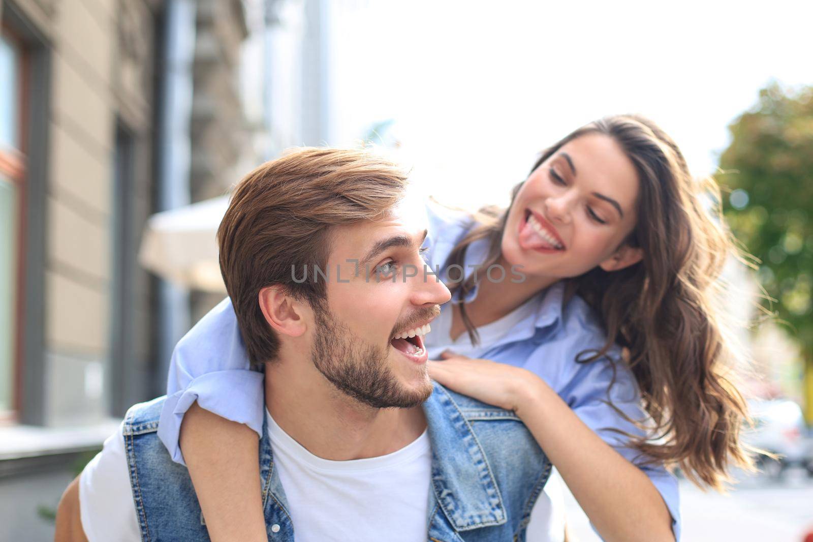 Handsome young man carrying young attractive woman on shoulders while spending time together outdoors