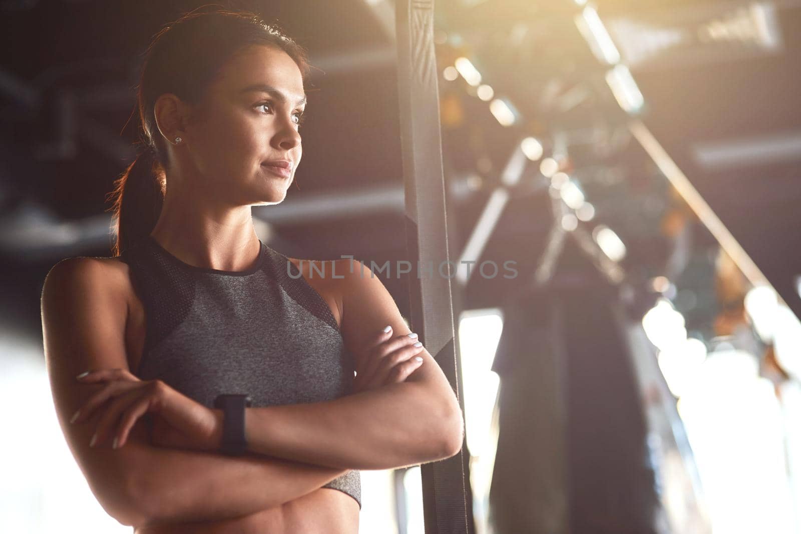 Fitness girl. Young attractive fit woman wearing sportswear keeping arms crossed and looking away while standing at gym. Sport, workout, wellness and healthy lifestyle