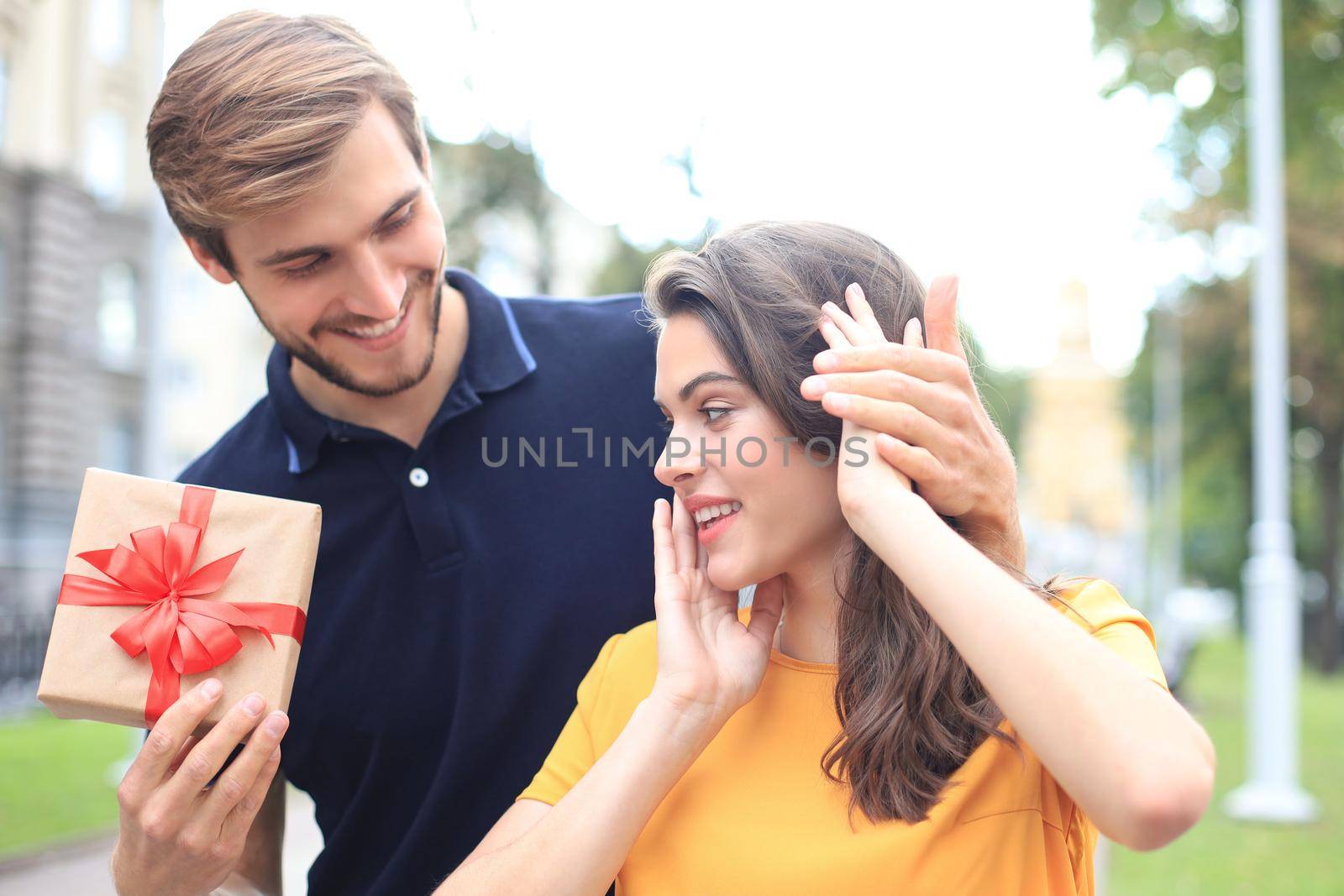 Image of charming excited couple in summer clothes smiling and holding present box outdoor