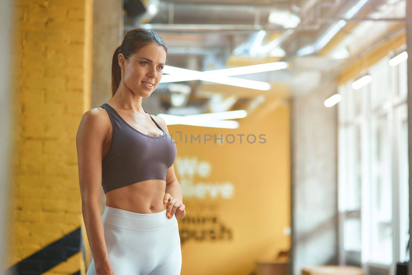 Young attractive fitness woman in sportswear with perfect body looking aside while standing at gym. Sport, training and healthy lifestyle concept