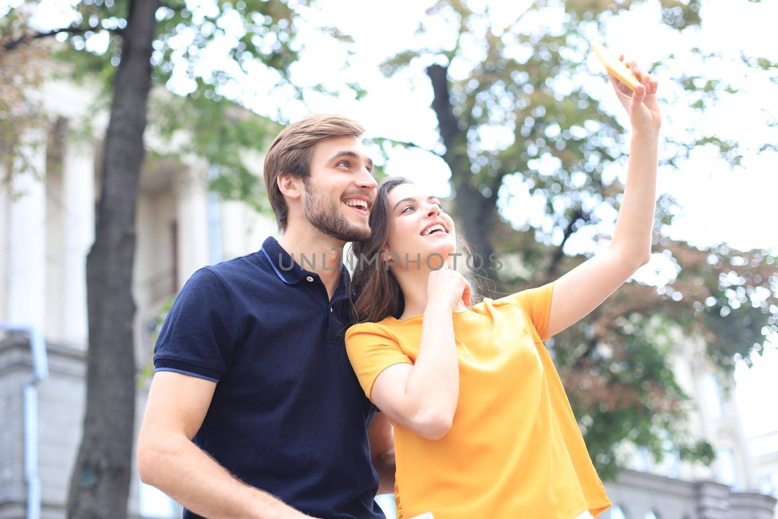 Beautiful lovely young couple walking at the city streets, hugging while taking a selfie