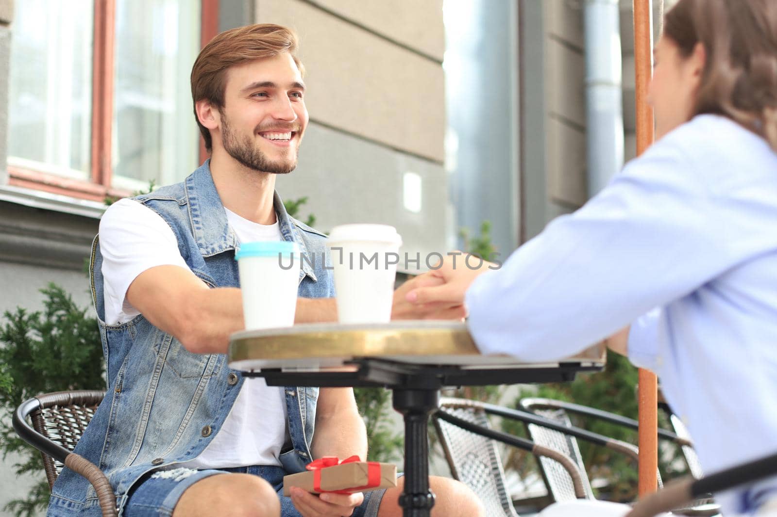 Smiling young girl having a date with her boyfriend at the coffee shop, man holding present box