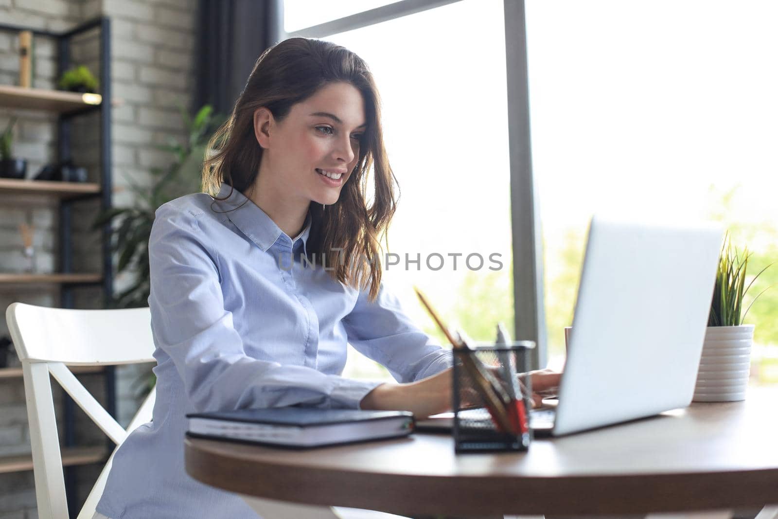 Smiling pretty woman sitting at table, looking at laptop screen. Happy entrepreneur reading message email with good news, chatting with clients online