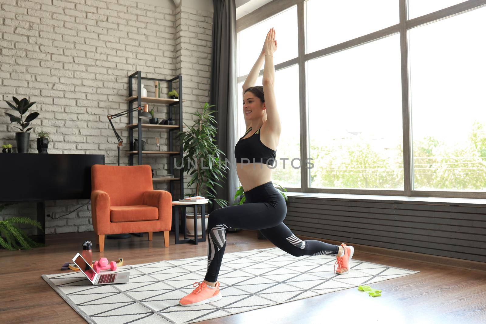 Fitness woman doing forward lunge exercises and watching online tutorials on laptop, training in living room. Stay at home activities. by tsyhun