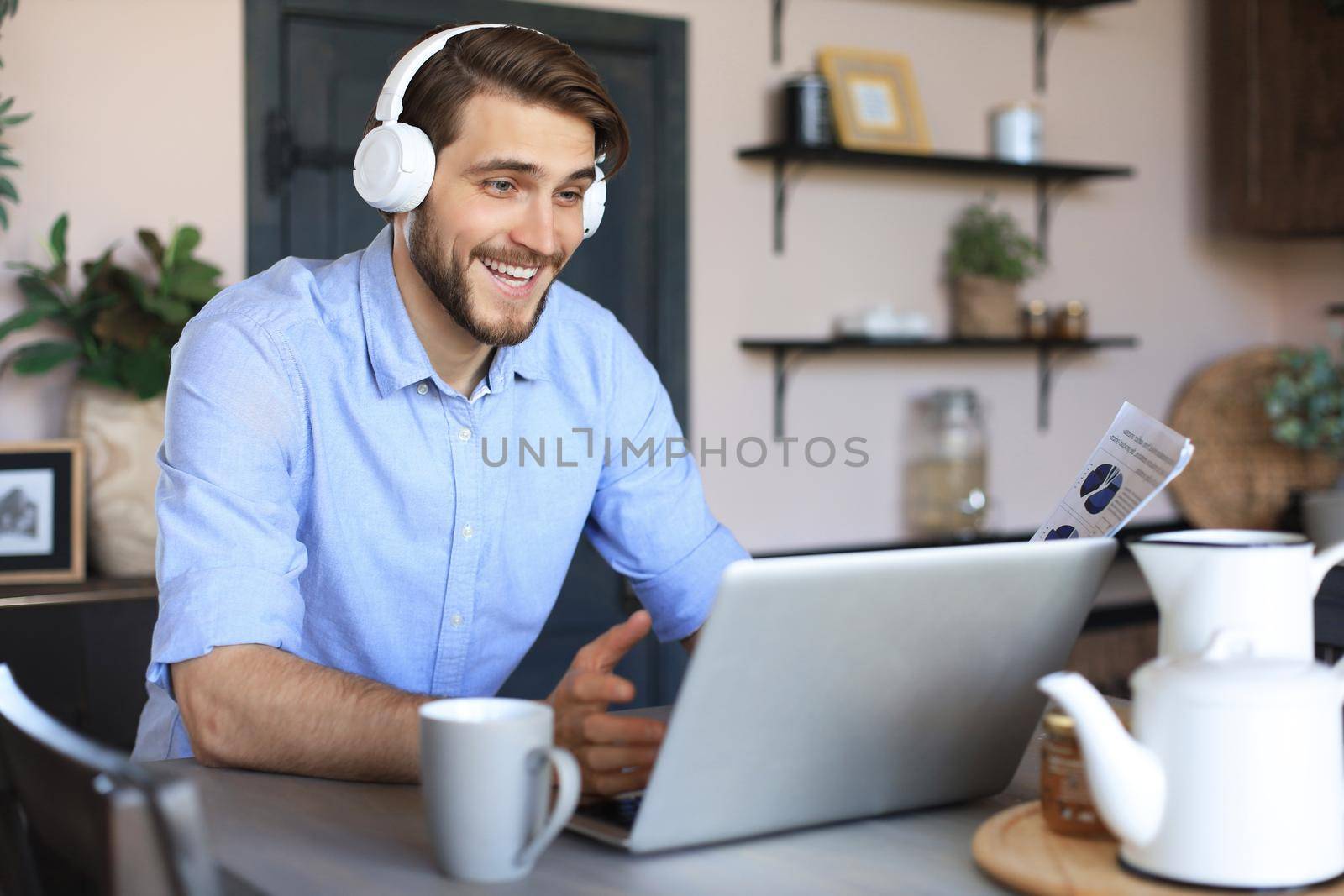 Smiling businessman greeting colleagues in video conference and negotiating distantly from home