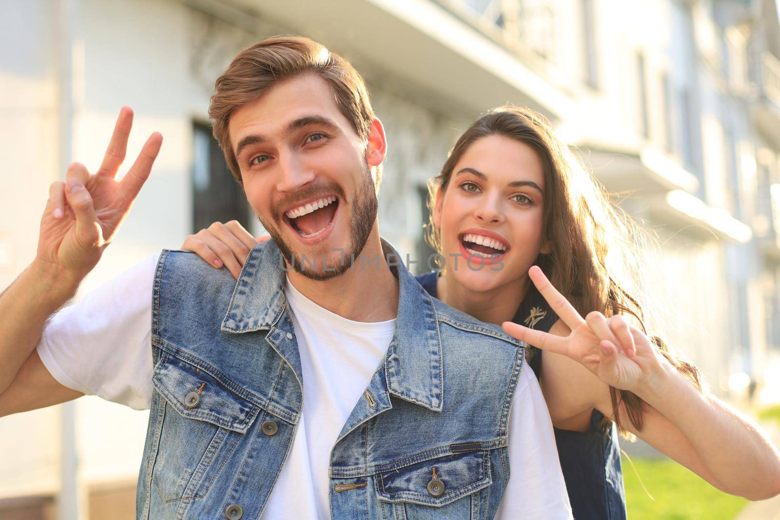 Image of a happy smiling cheerful young couple outdoors take a selfie by camera showing peace