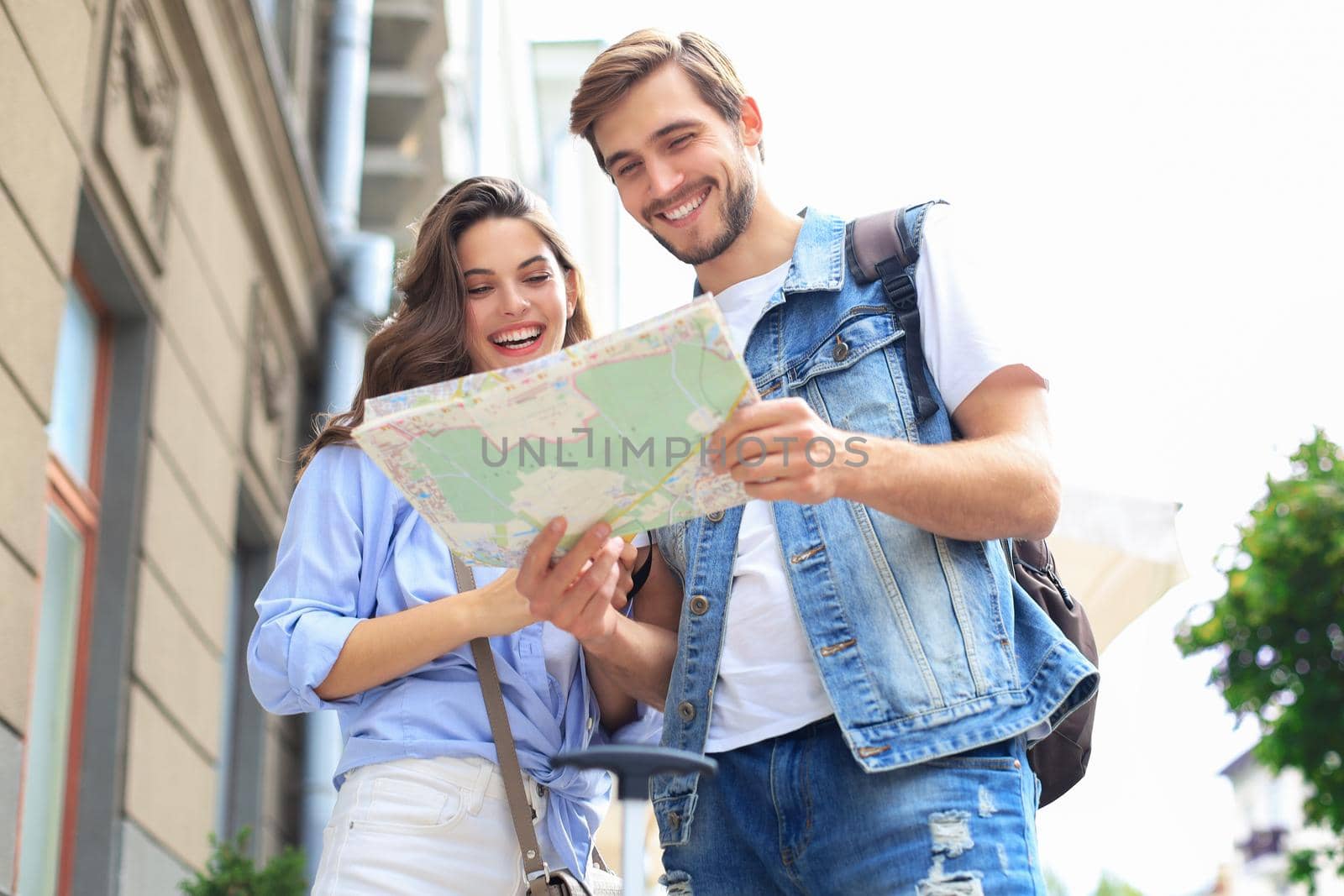 Beautiful young couple holding a map and smiling while standing outdoors