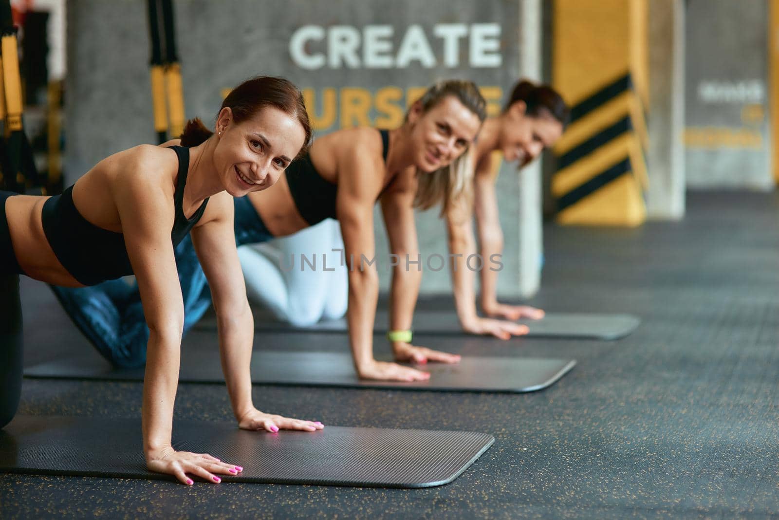 Sport is our life. Three young happy sportive women smiling at camera while exercising with trx fitness straps at gym. Suspension training, workout, wellness and healthy lifestyle