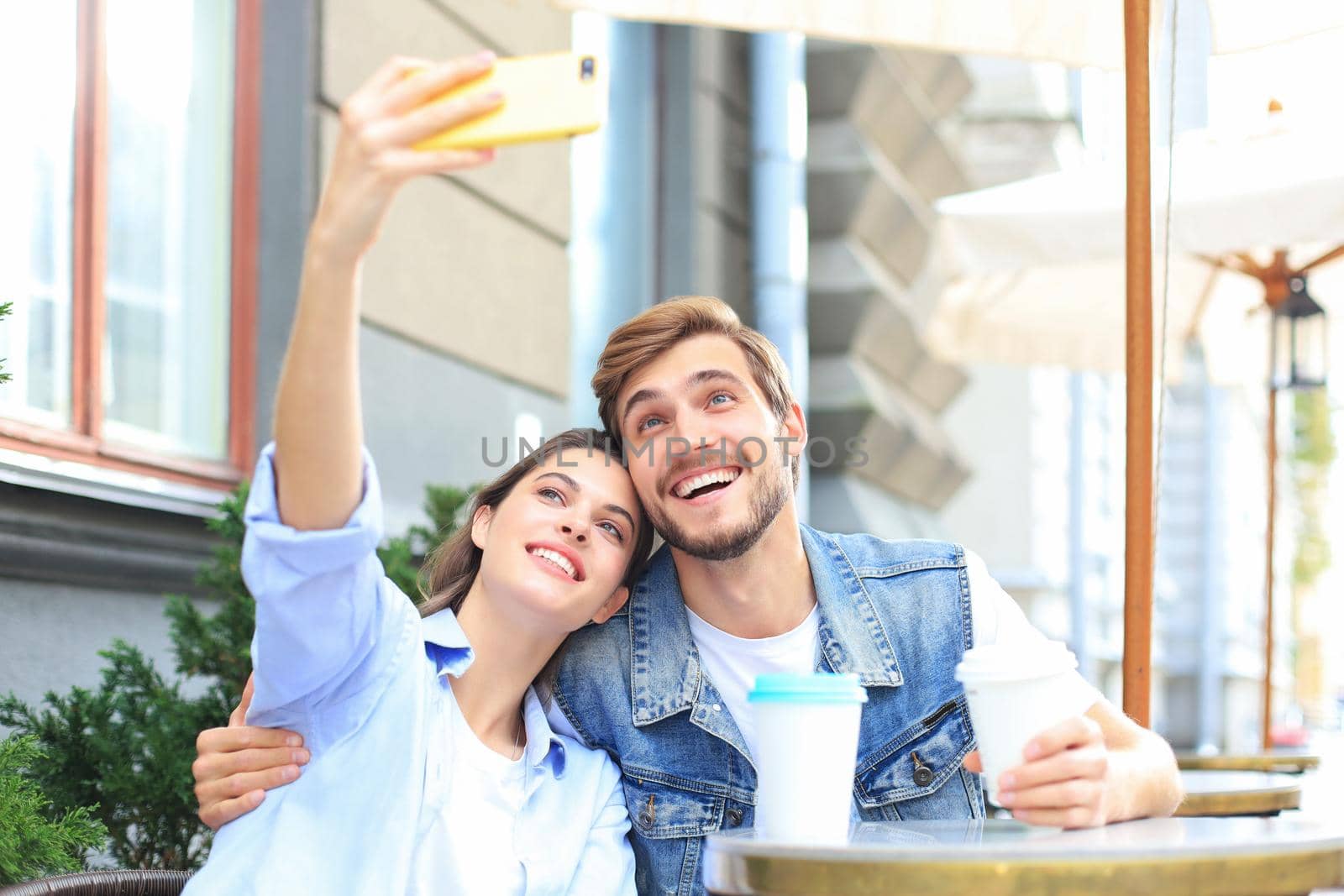 Beautiful young loving couple bonding to each other in cafe while woman making selfie by smart phone