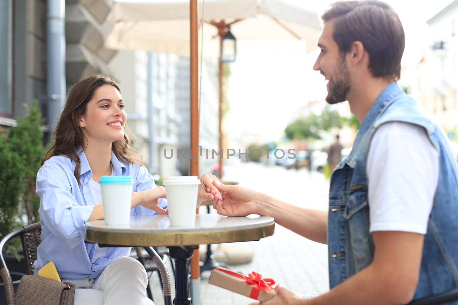 Smiling young girl having a date with her boyfriend at the coffee shop, man holding present box