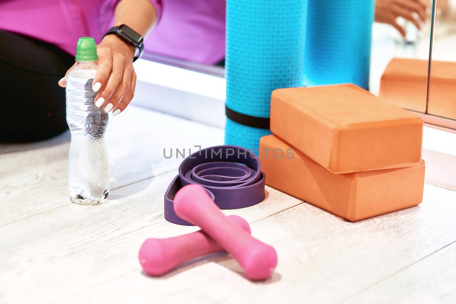 Fitness equipment. Dumbbells, yoga mat, resistance band and yoga bricks on wooden floor in studio by friendsstock