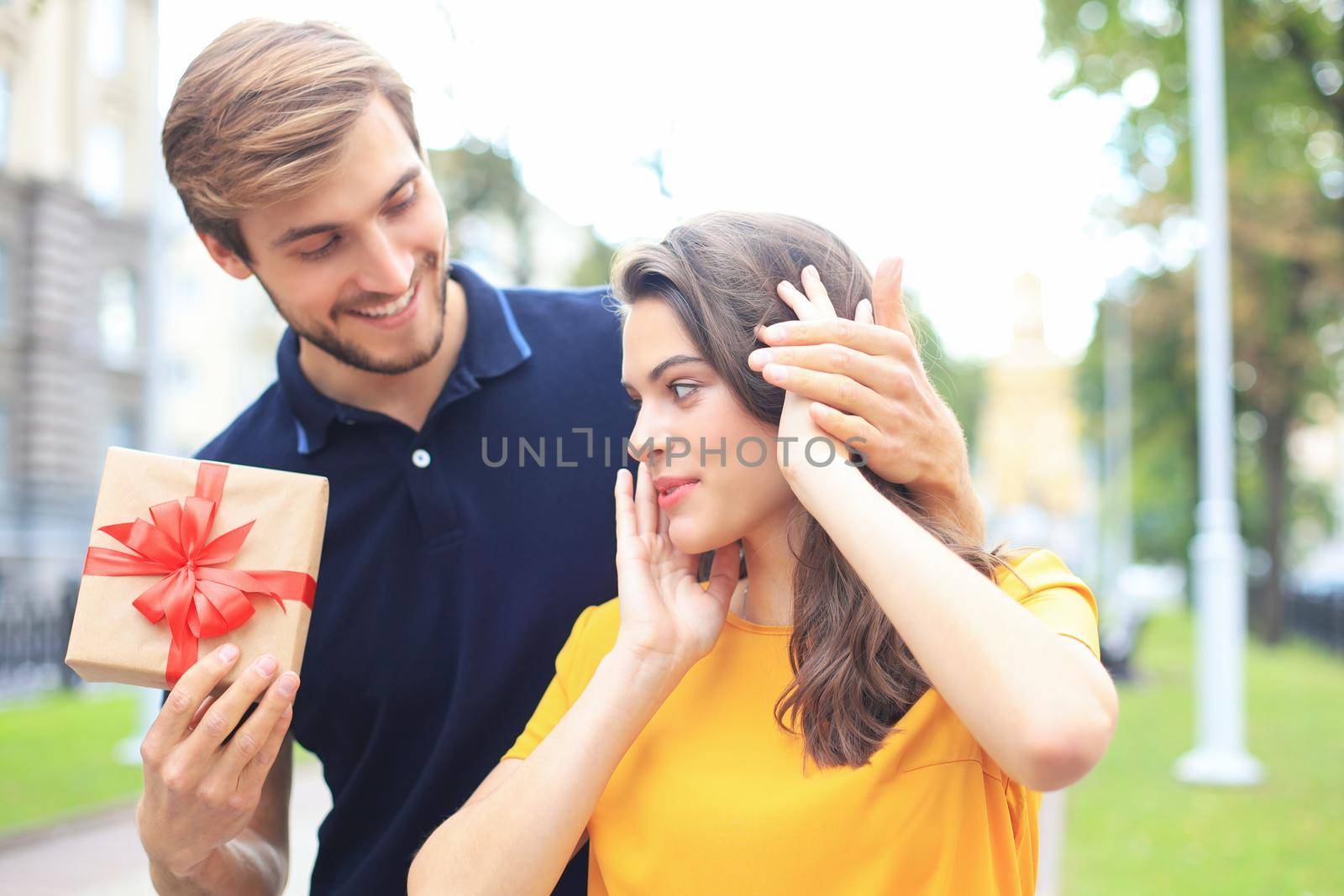 Image of charming excited couple in summer clothes smiling and holding present box outdoor