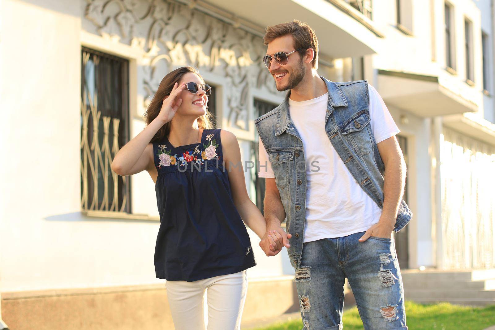 Image of lovely happy couple in summer clothes smiling and holding hands together while walking through city street