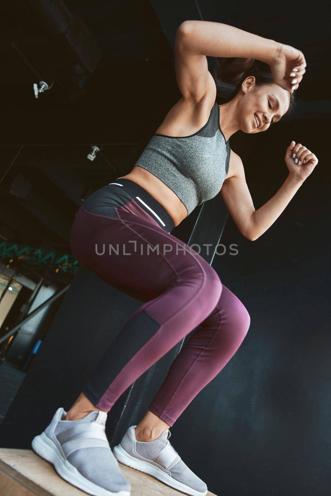 Best calorie burning Exercises. Bottom view of a strong athletic woman in sportswear doing box jump while working out at industrial gym, vertical shot. Sport, wellness and healthy lifestyle