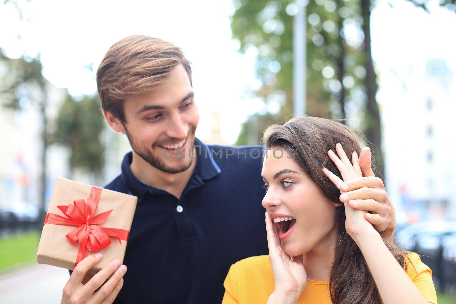 Image of charming excited couple in summer clothes smiling and holding present box outdoor