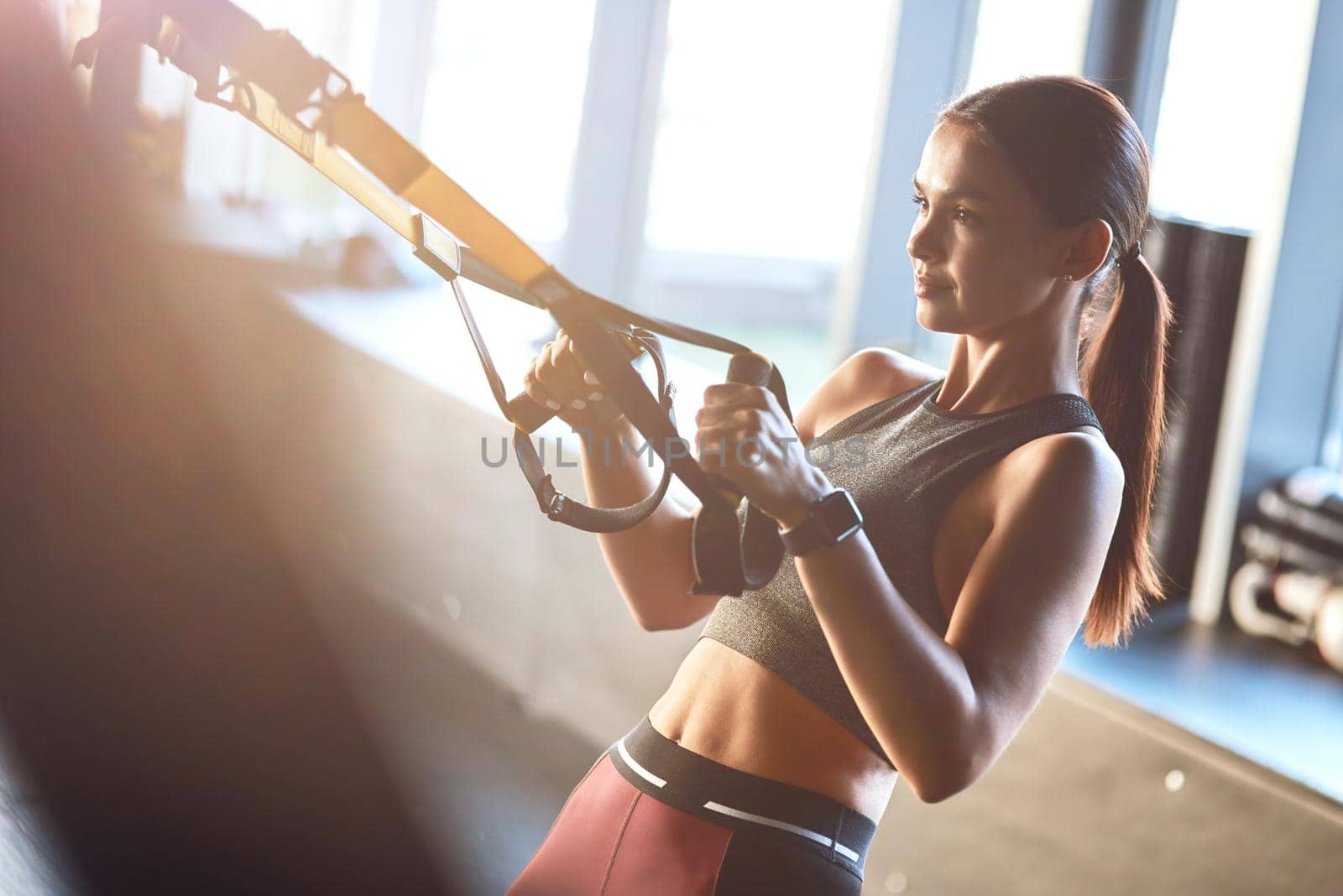 Side view of a young strong and fit woman exercising with fitness trx straps at gym. Sport, workout, wellness and healthy lifestyle