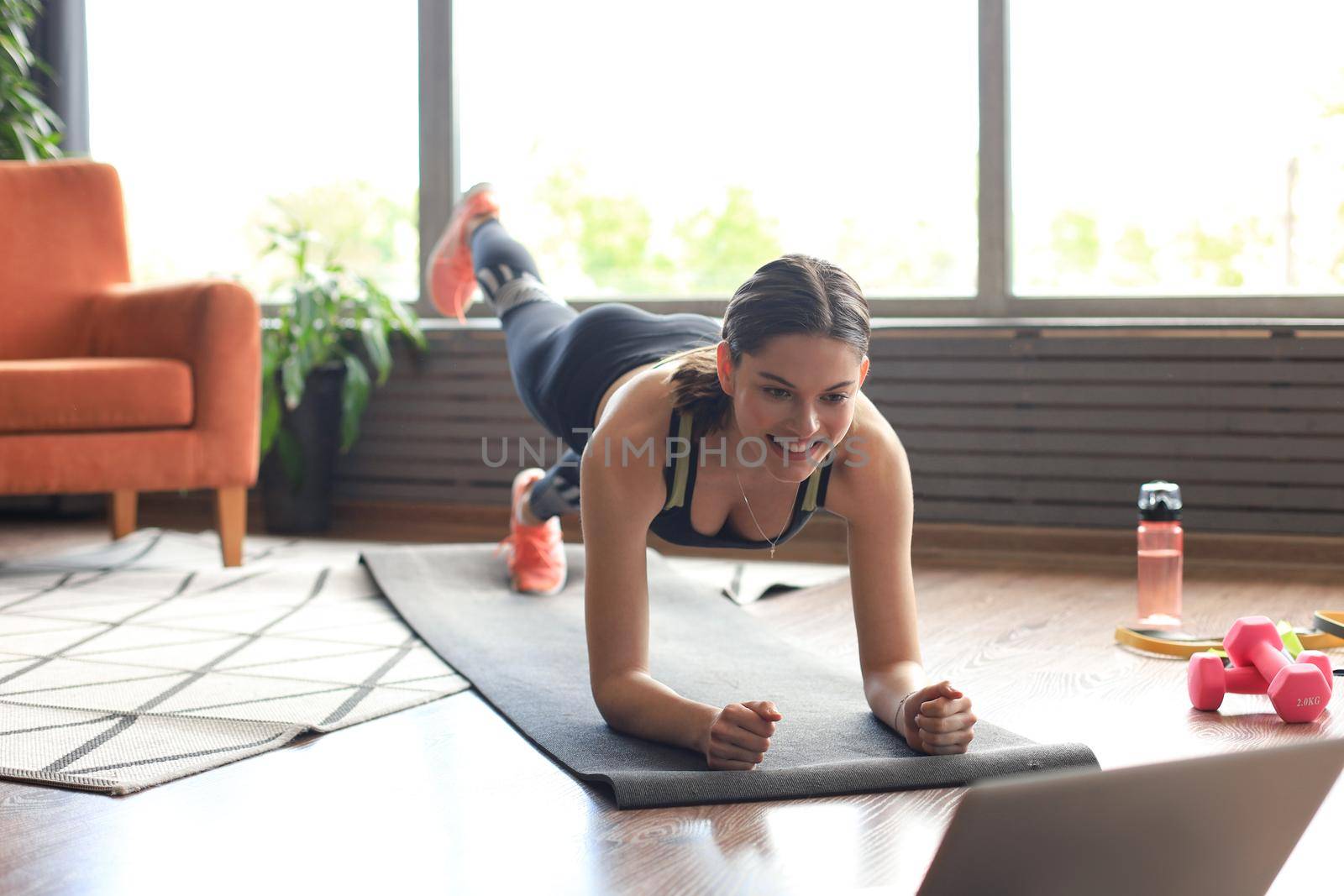 Beautiful fitness woman doing a plank exercise watching online tutorials on laptop, training in living room. Healthy lifestyle. Girl goes in for sports at home.