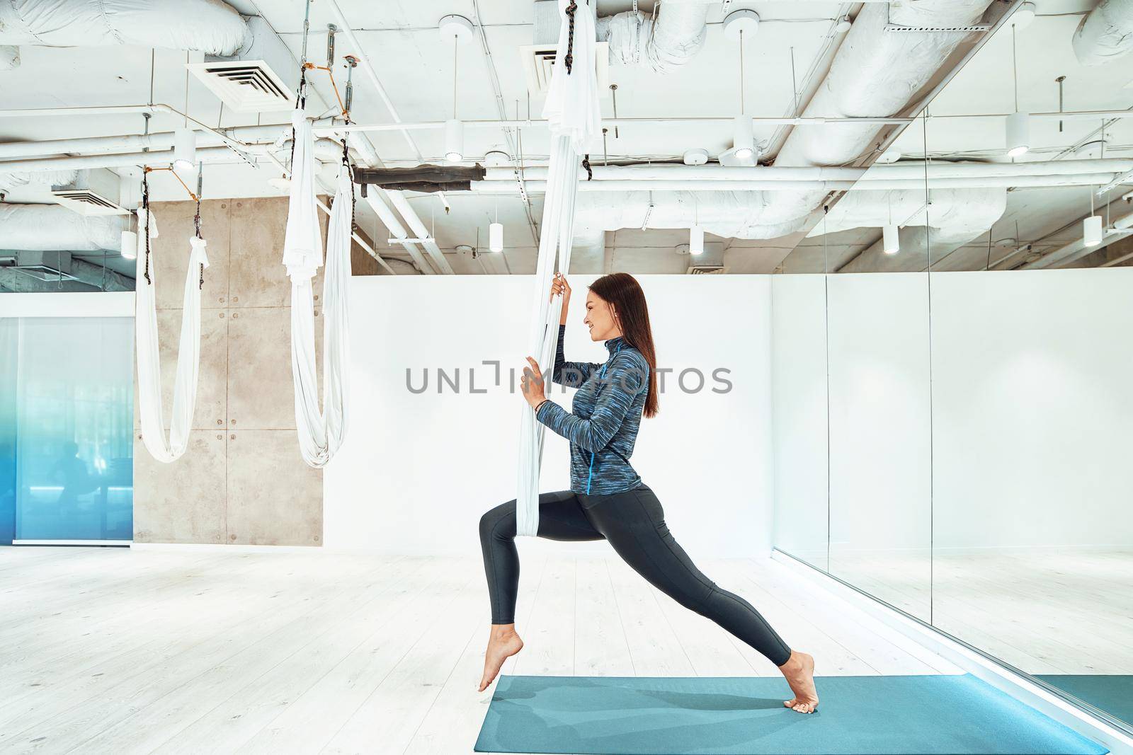 Antigravity. Young caucasian fitness woman in sportswear practicing fly yoga in beautiful bright studio by friendsstock