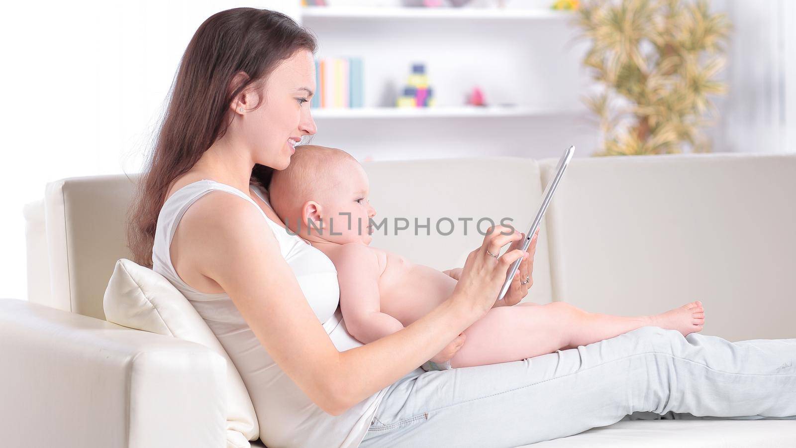 mother and baby are looking to play and read tablet computer on the couch at home