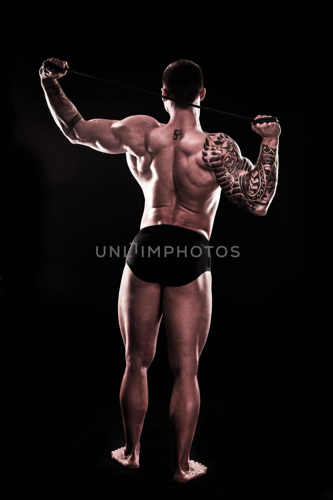 rear view. A muscular man performs exercises using a resistance band. isolated on black background