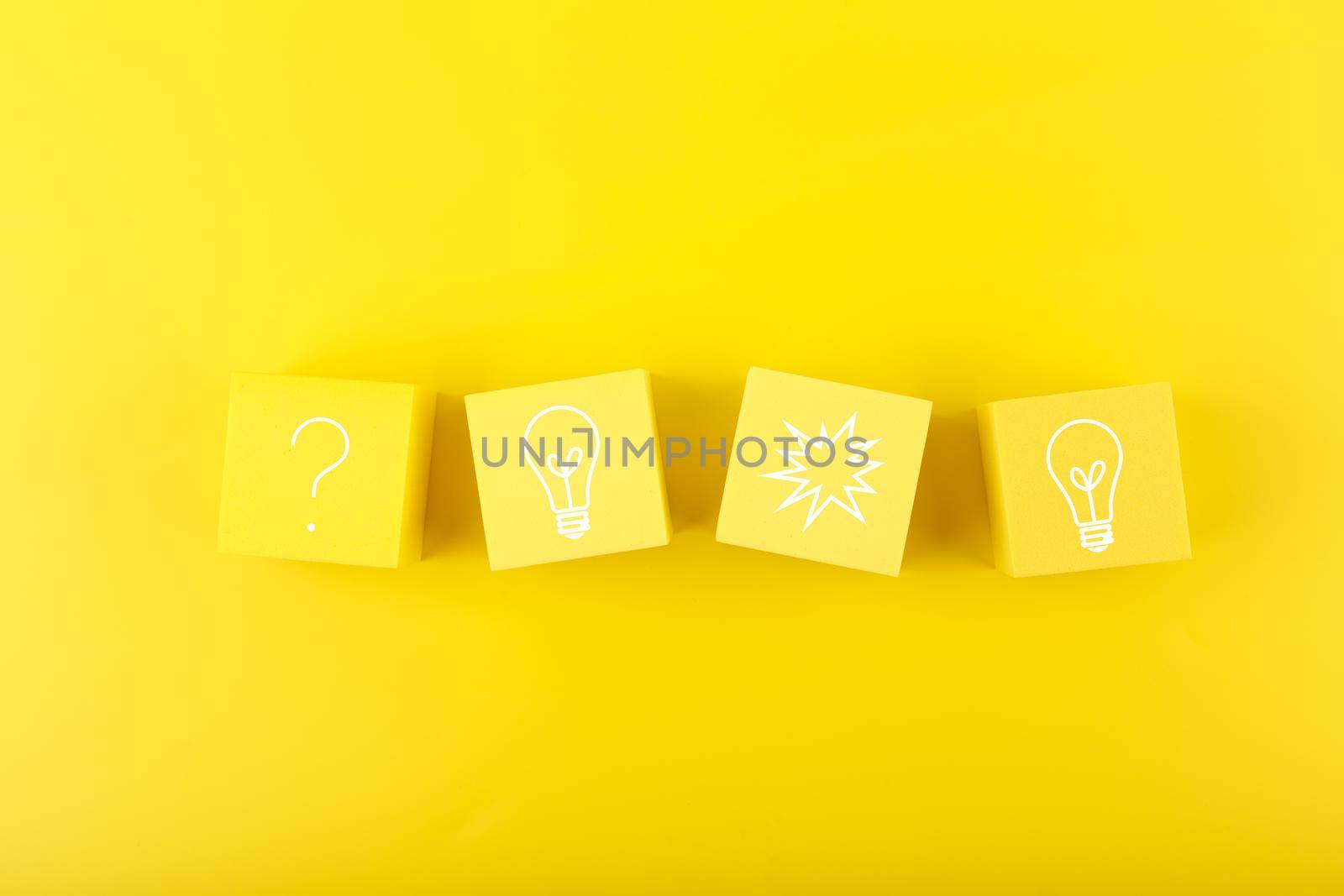 Concept of idea, creativity, start up or brainstorming. Light bulb and question signs drawn on toy cubes on yellow background