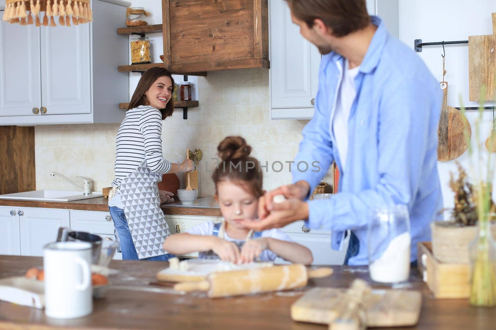 Cute little girl and her parents are having fun while cooking in kitchen at home together