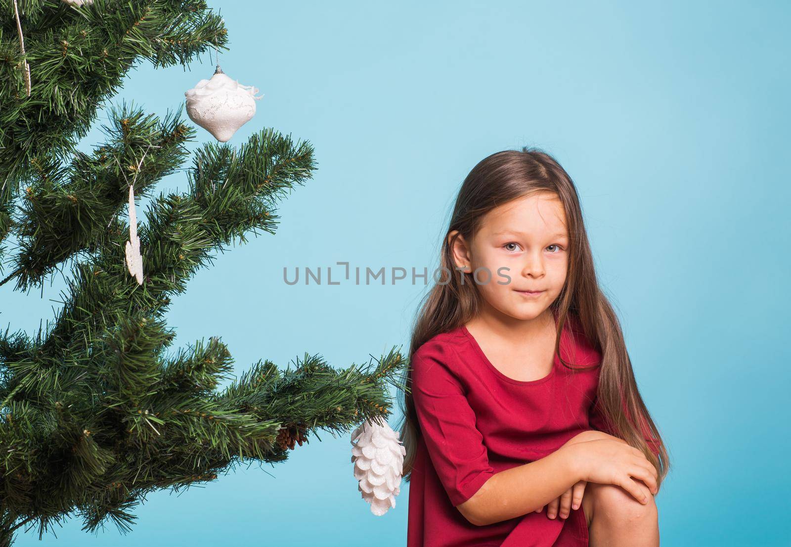 Little girl with christmas tree on blue background.