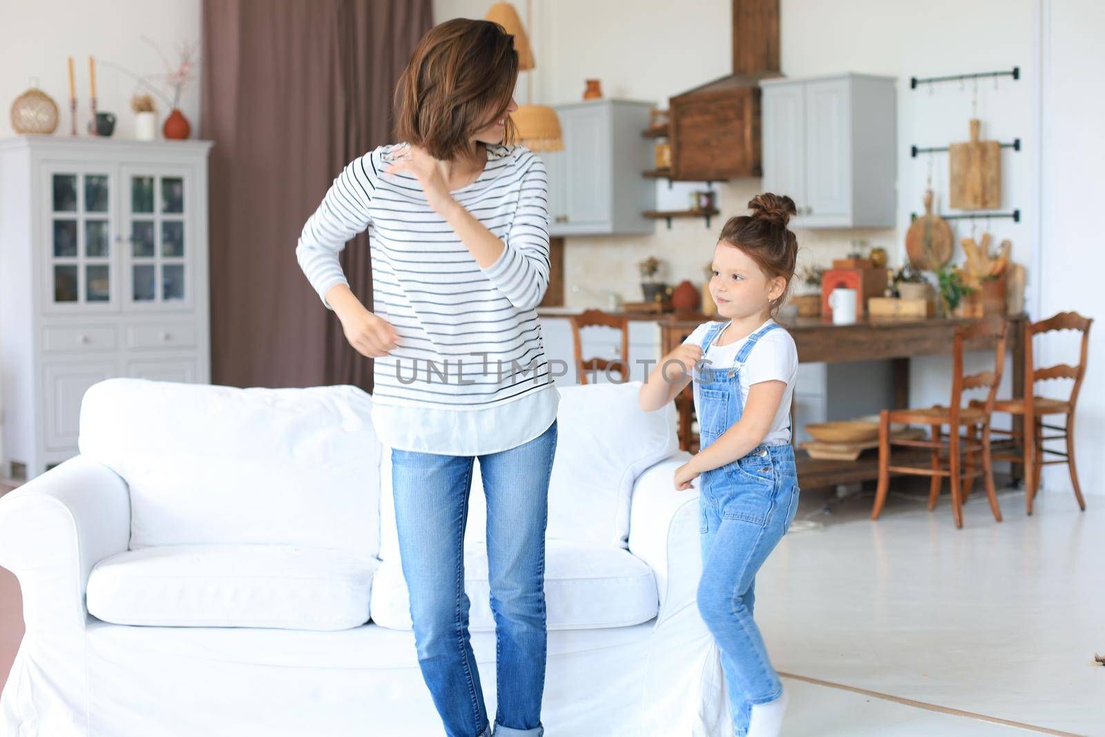 Cheerful mother with little daughter dancing at favourite song in living room at home. by tsyhun