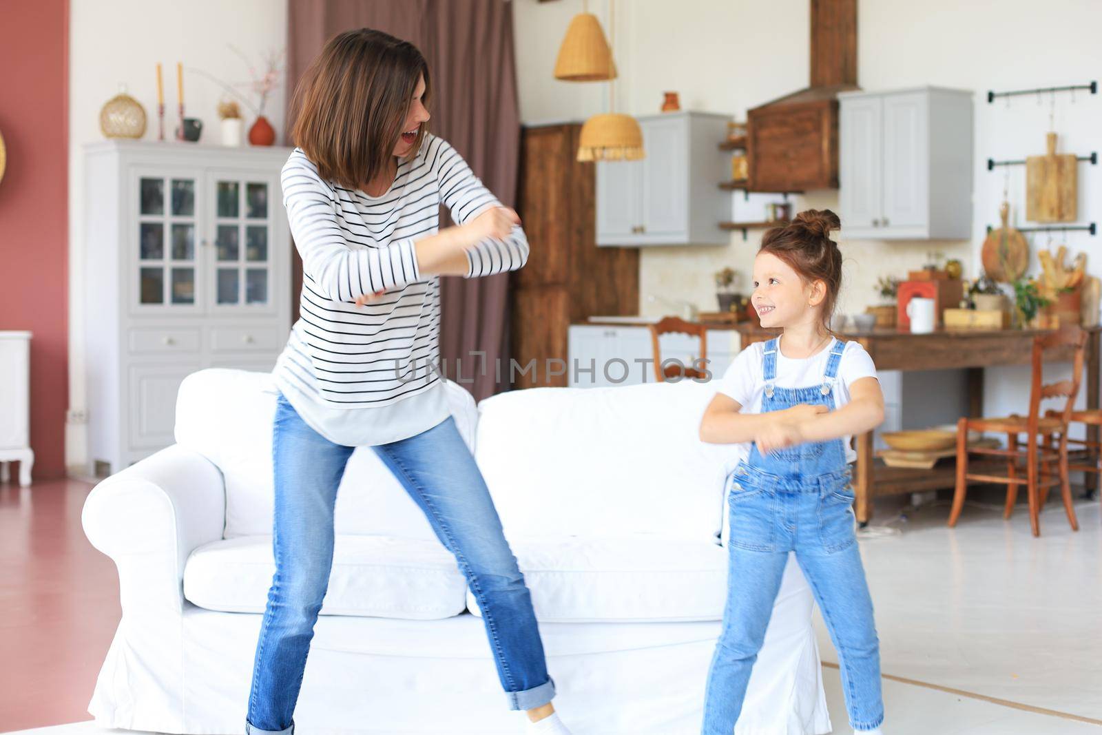 Cheerful mother with little daughter dancing at favourite song in living room at home