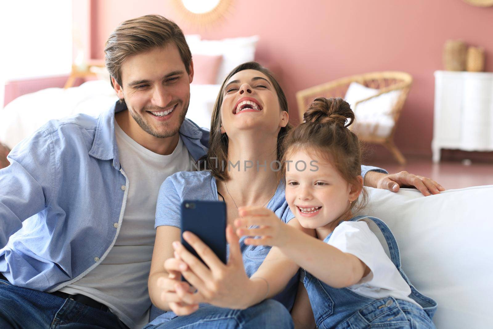 Beautiful young family with little child taking a selfie with a smartphone at home on the couch
