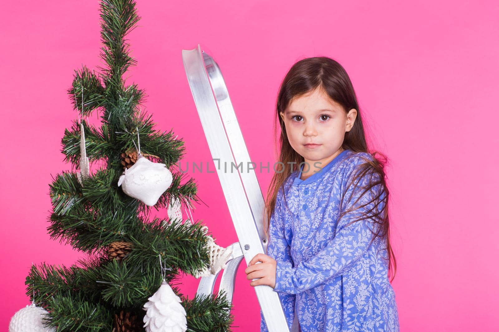 Christmas and holiday concept - A little girl is decorating Christmas tree