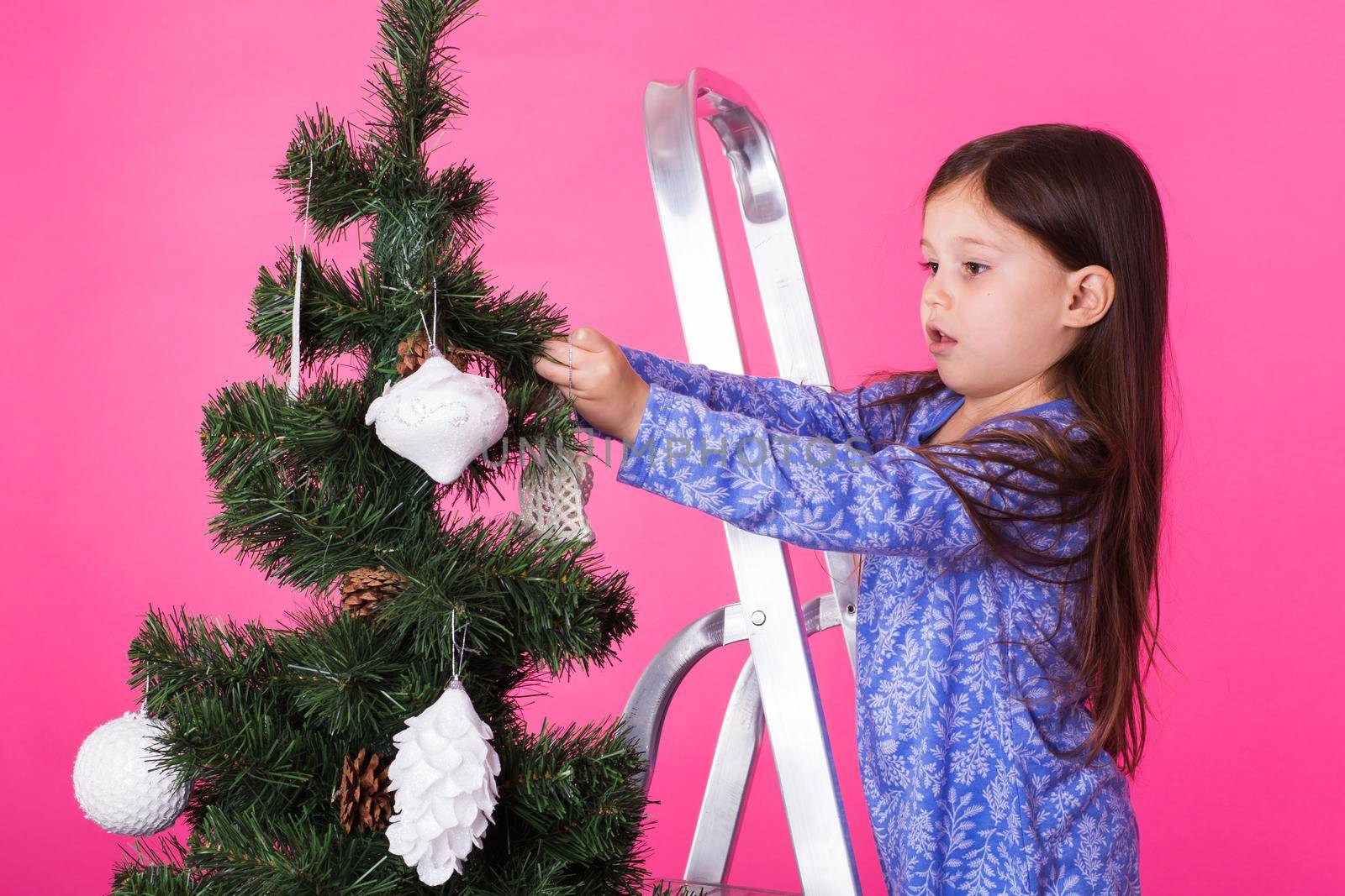 Little girl with christmas tree on pink background.