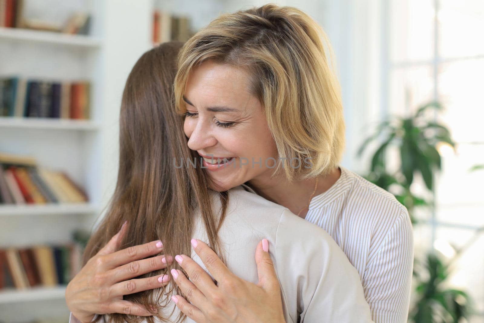 Cheerful young woman is embracing her middle aged mother in living room