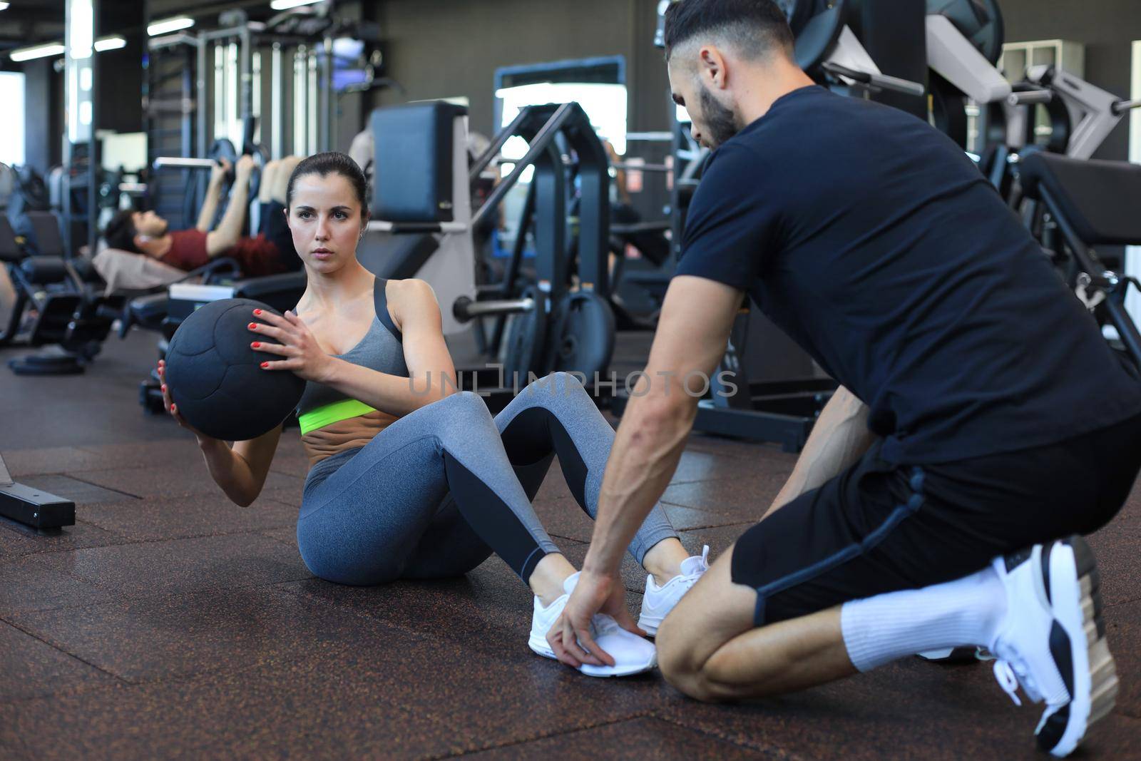 Trainer helping young woman to do abdominal exercises in gym
