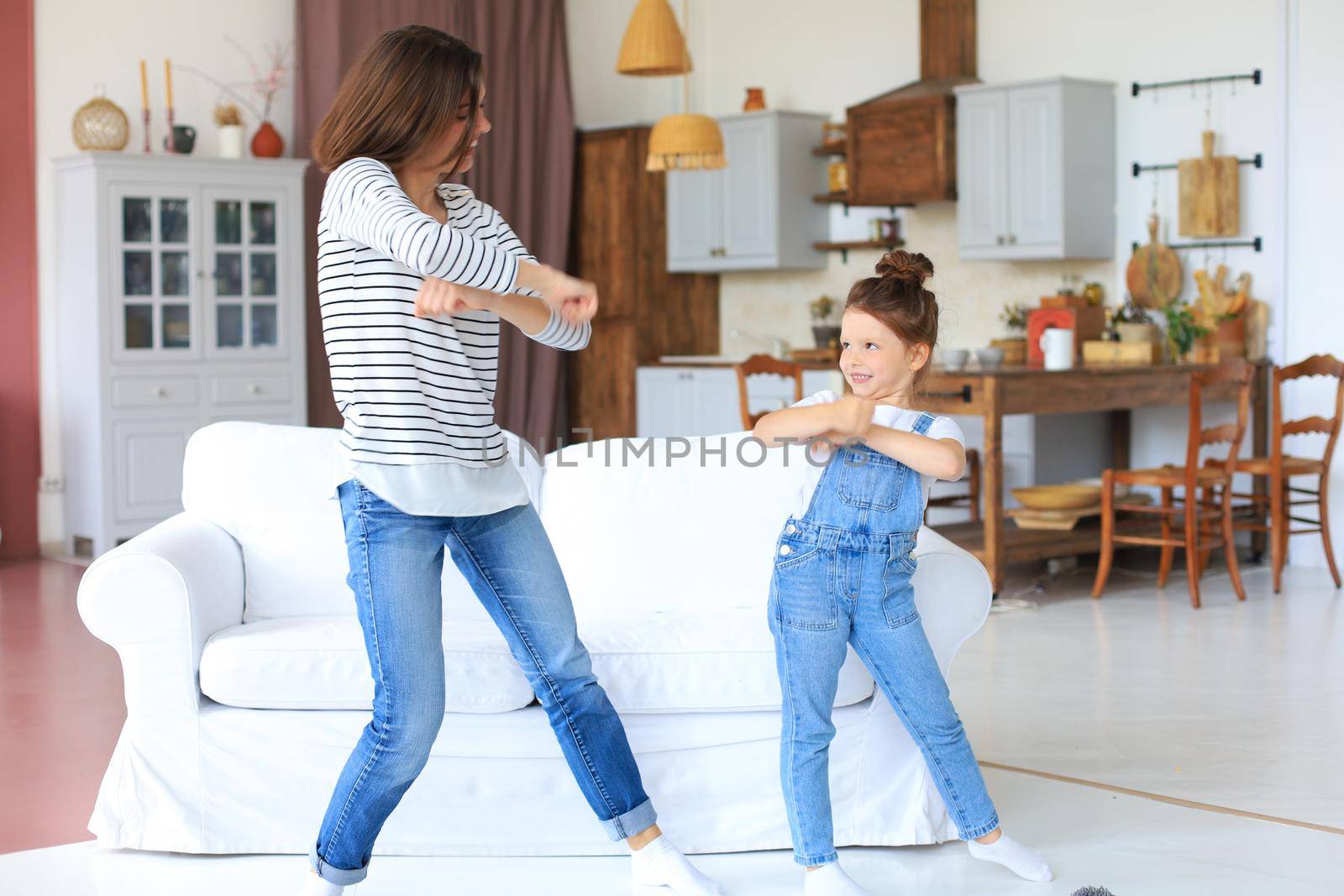 Cheerful mother with little daughter dancing at favourite song in living room at home