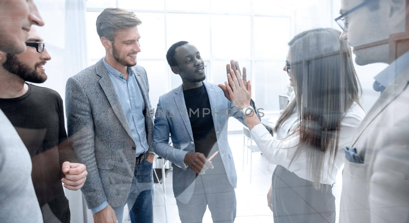 Group of young colleagues giving each other a high five while standing in an office