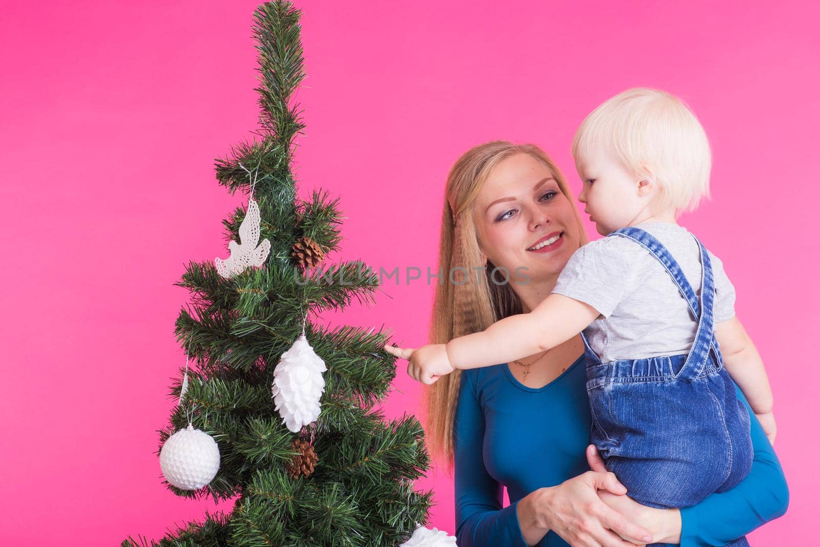 Holidays, family and christmas concept - young mom with her little daughter near christmas tree on pink background by Satura86