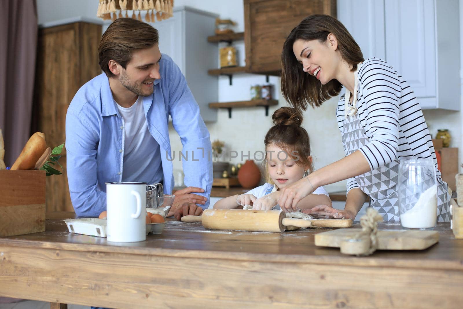 Cute little girl and her parents are having fun while cooking in kitchen at home together