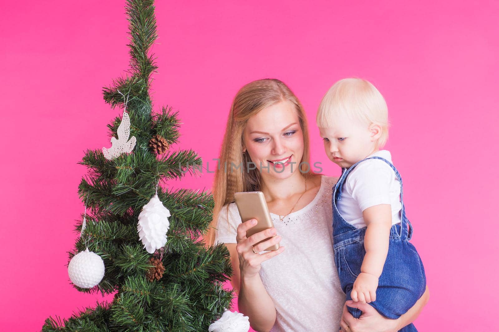 Mother and little daughter taking a selfie near Christmas tree.