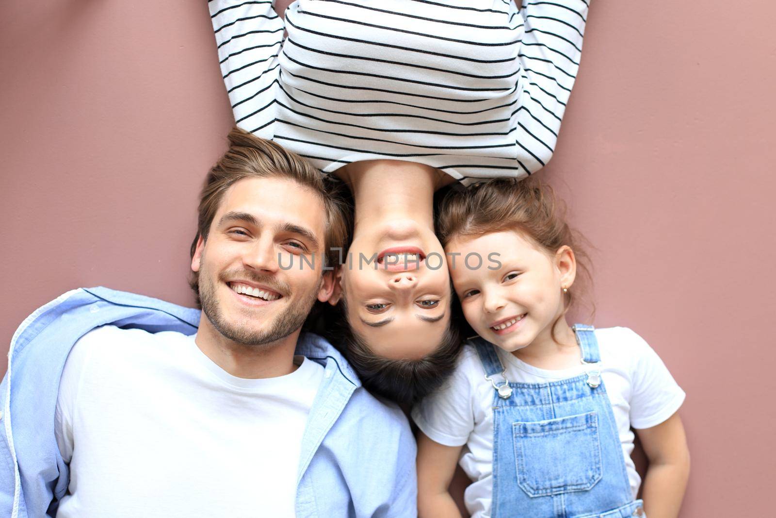 Top view portrait of smiling young parents with little preschooler daughter lying relaxing on warm floor at home, happy family with small child rest have fun at home