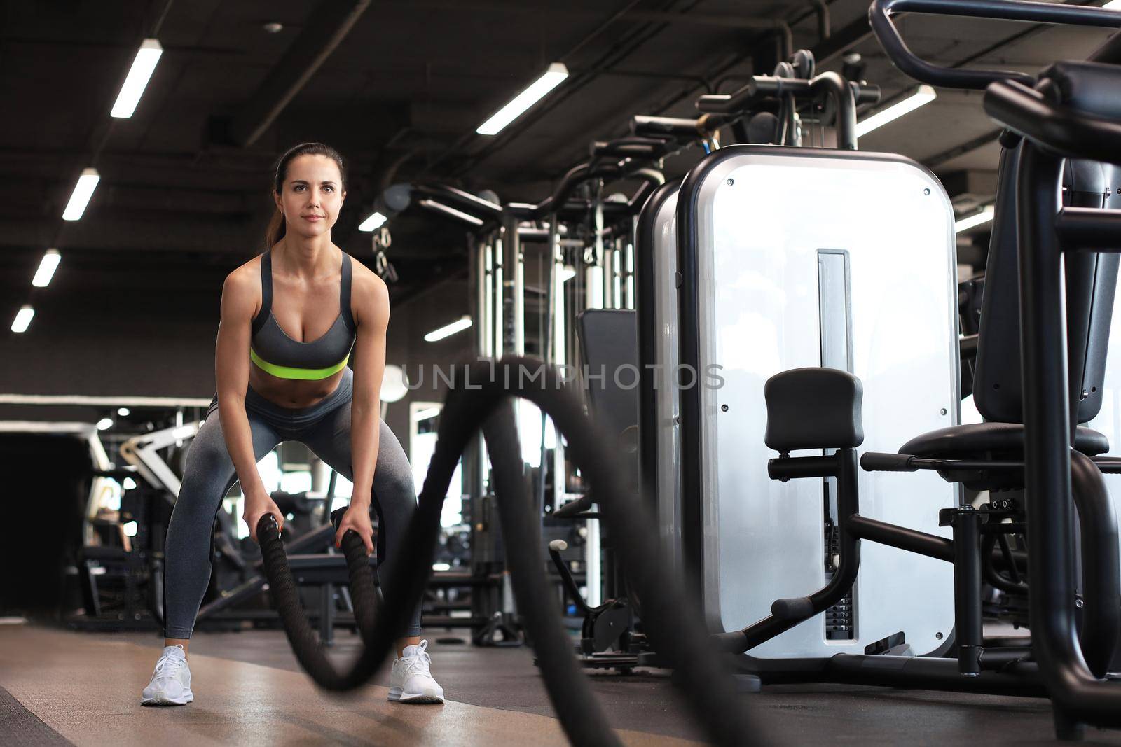 Fit woman using battle ropes during strength training at the gym