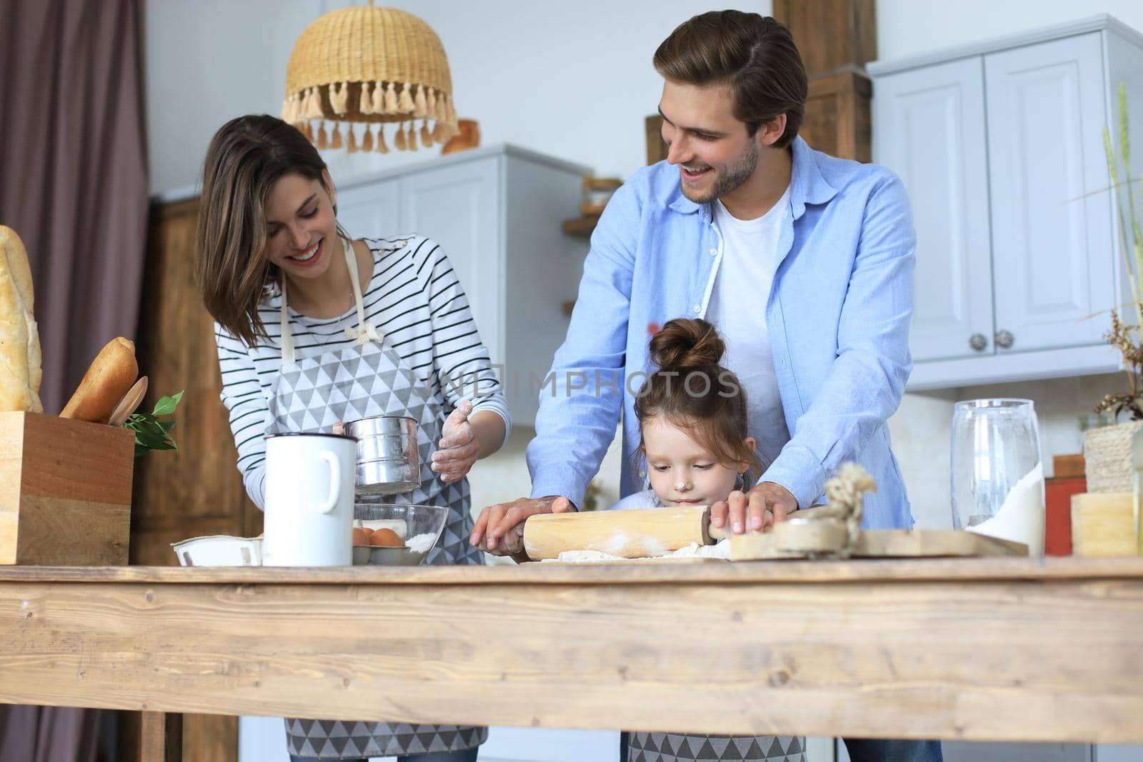 Cute little girl and her parents are having fun while cooking in kitchen at home together