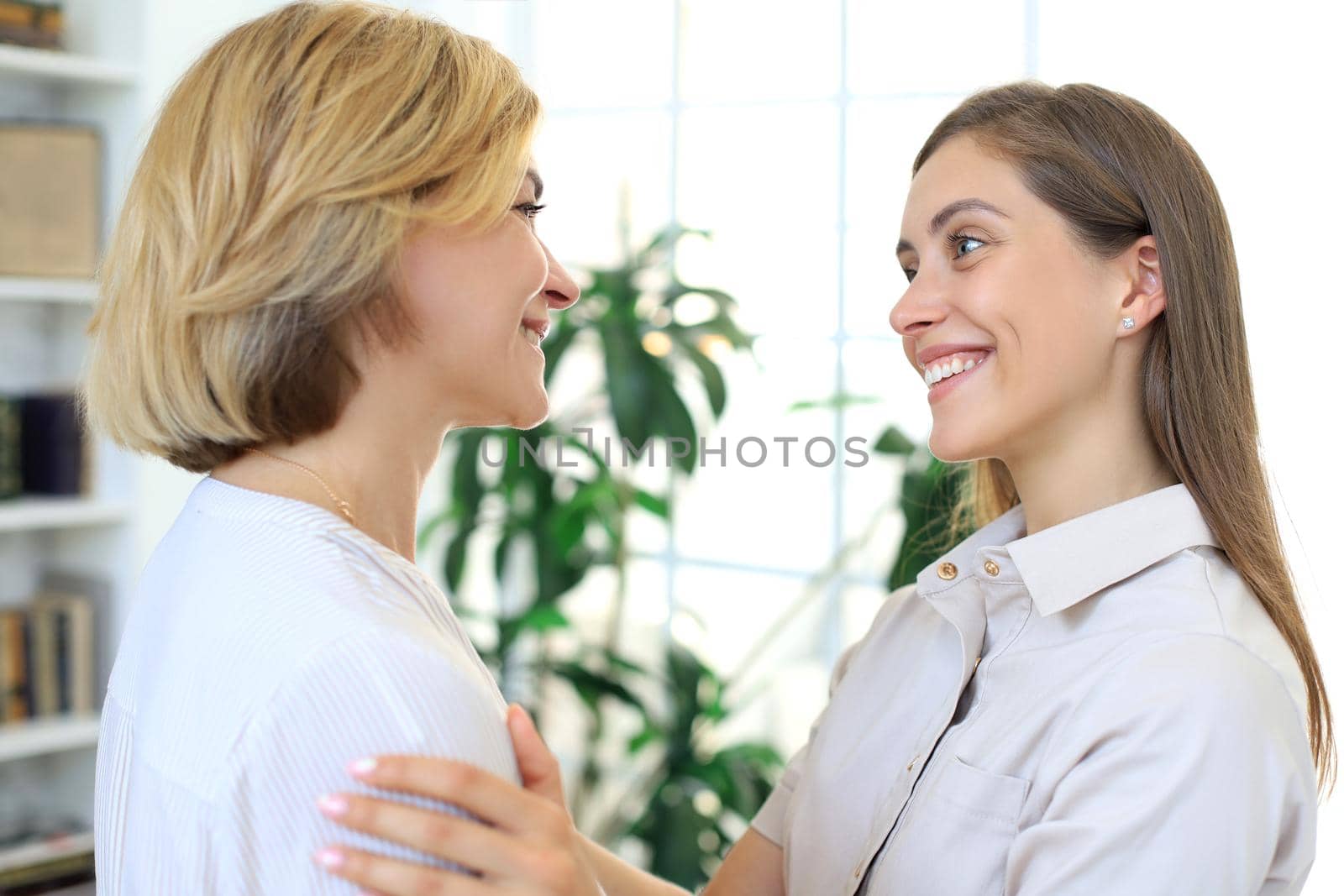 Cheerful young woman is embracing her middle aged mother in living room