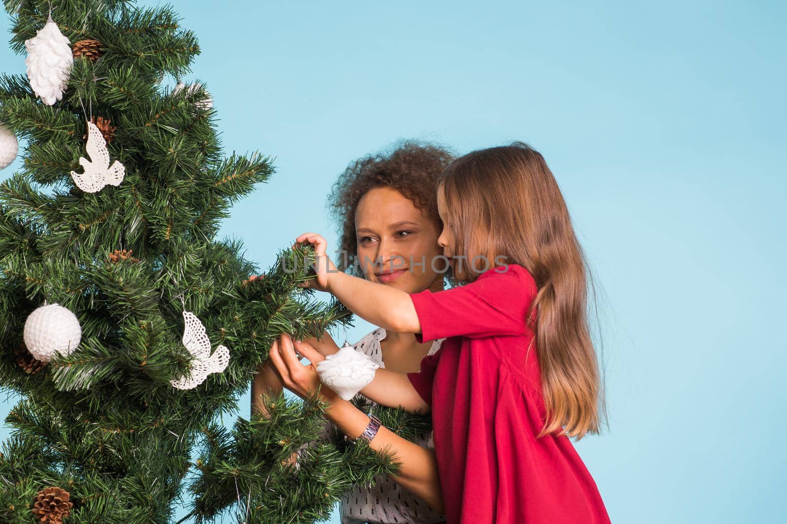 people, family and christmas concept - mother and daughter decorating christmas tree on blue background.