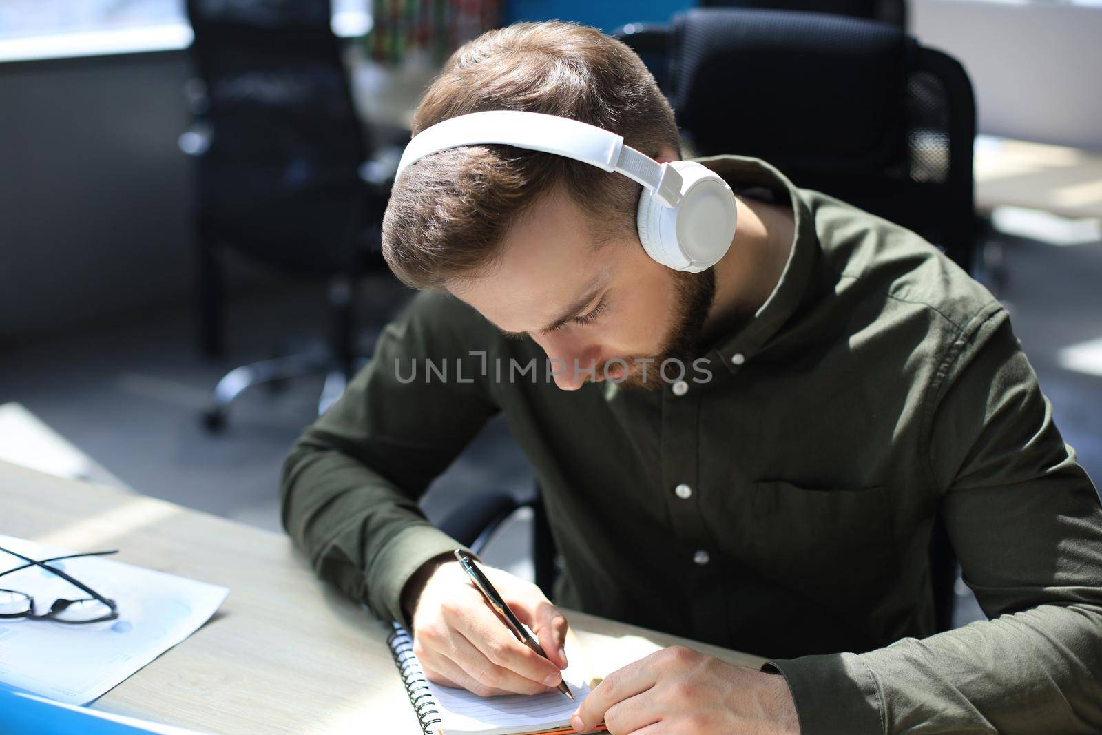 Thoughtful young business man writing something down while working in modern office