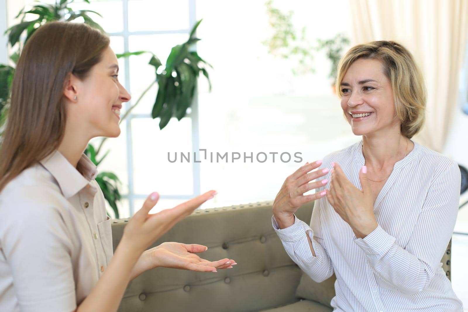 Happy middle aged mother and daughter talking on sofa in living room
