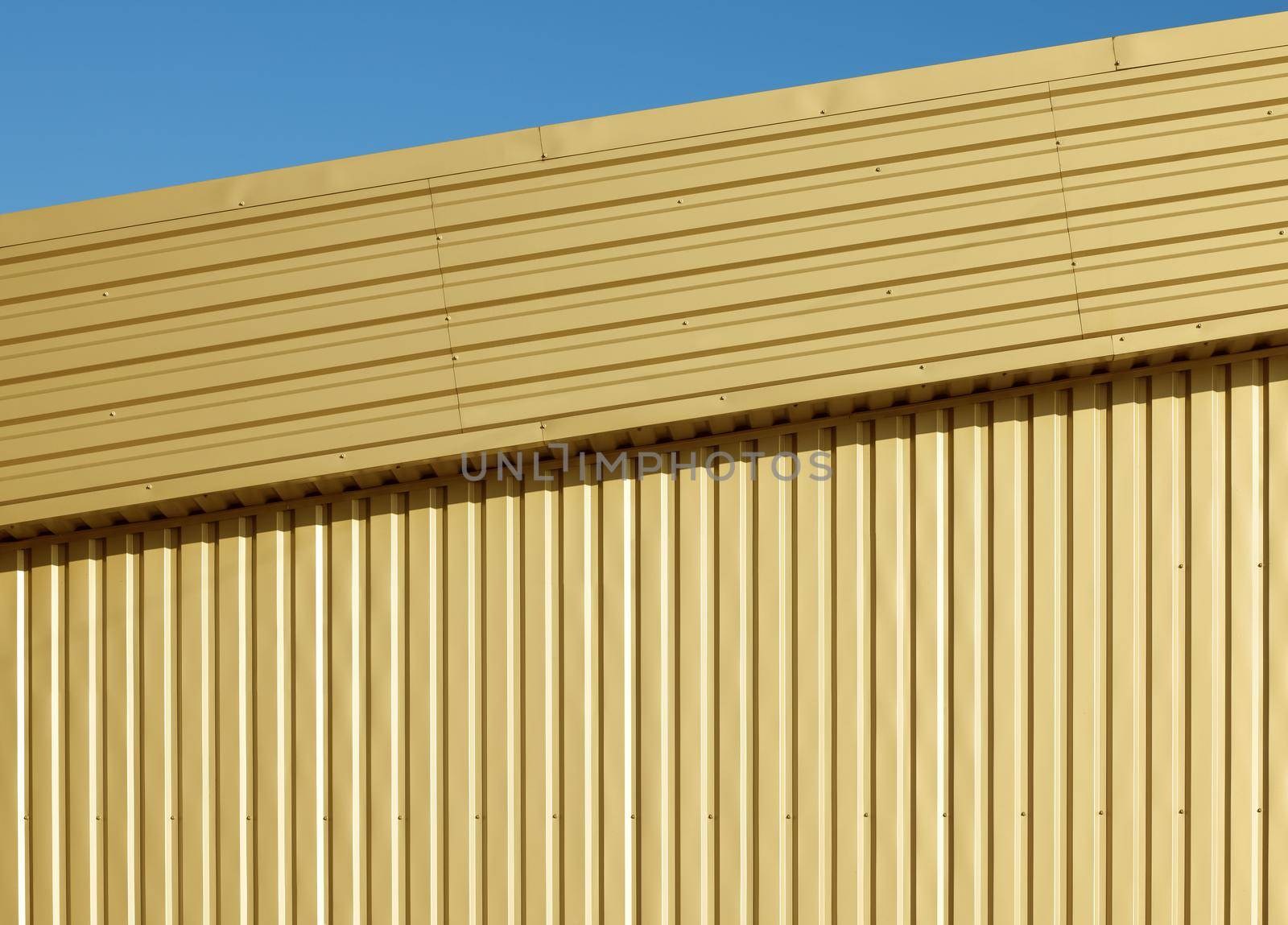 Background texture of golden aluminum corrugated goffered metal wall under blue sky