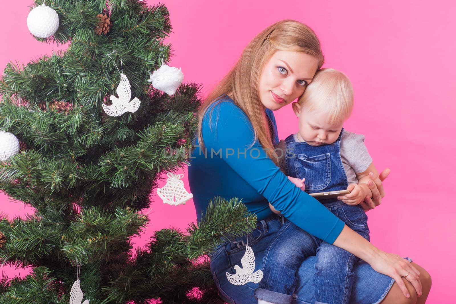 Holidays and people concept - Woman and her kid near christmas tree on pink background by Satura86