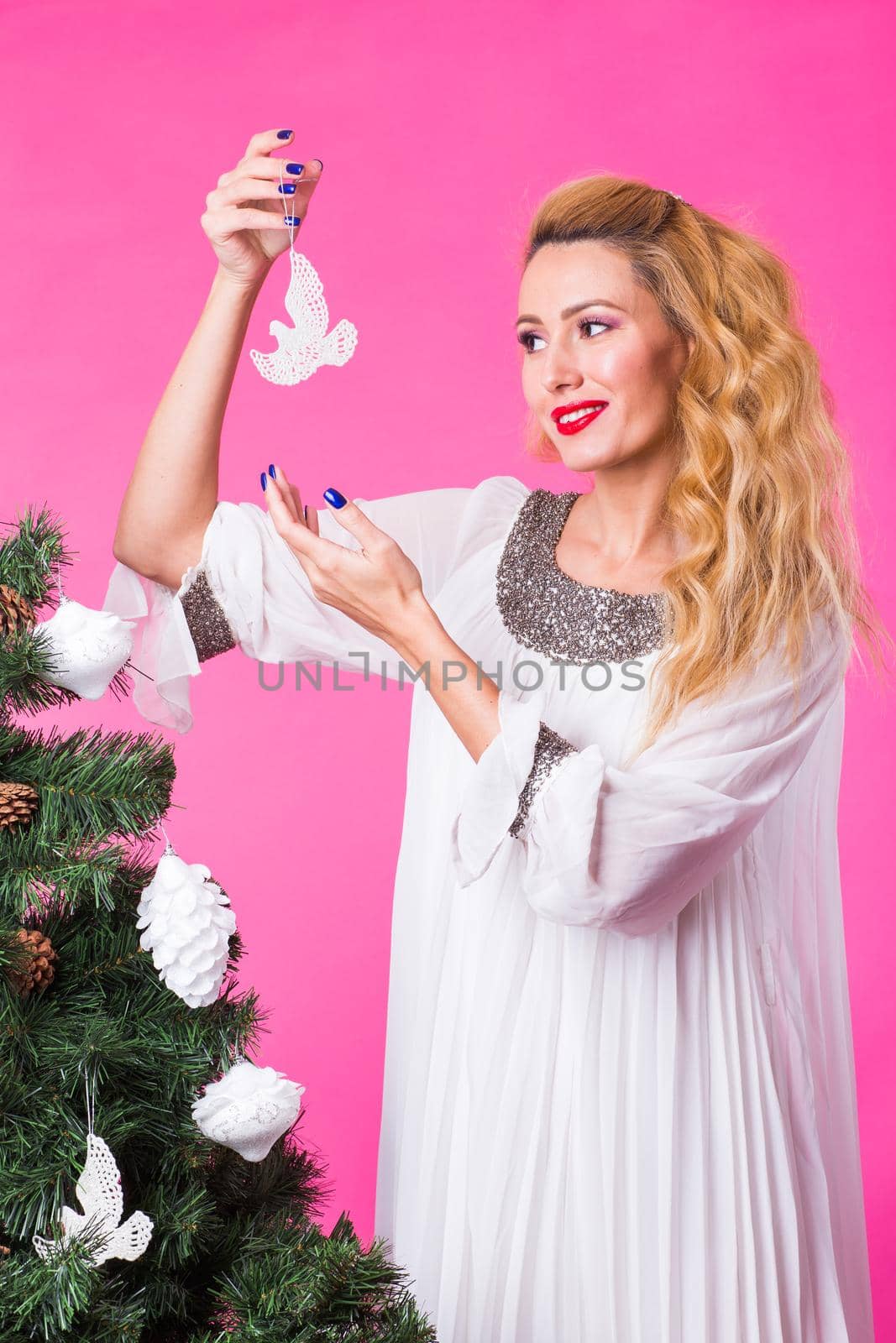 People, holidays and christmas concept - woman decorating christmas tree on pink background by Satura86